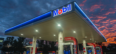 Estación de servicio Mobil al atardecer con el cielo nublado en una mitad y arrebol en la otra mitad.