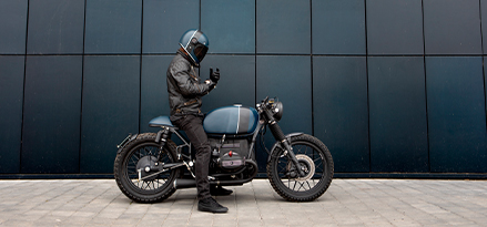 Motociclista con equipamiento de casco y chaqueta montado en una motocicleta BMW R100 de color azul