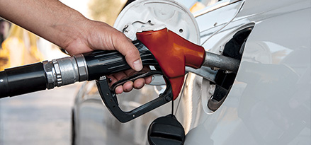 Boquilla de gasolina de color rojo para gasolina con mayor octanaje dentro de un tanque de gasolina de un vehículo blanco.