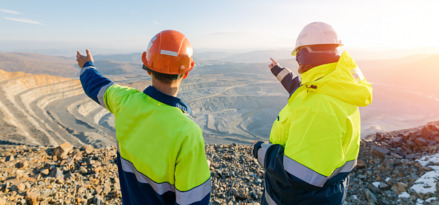 Dos ingenieros con chamarras de alta visibilidad señalando una mina abierta