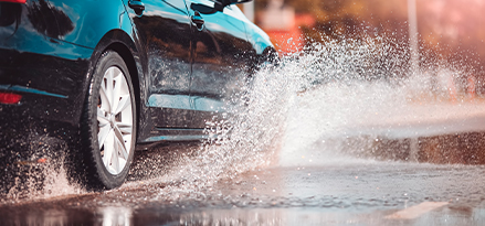 Automóvil que circula en una calle con lluvia y salpica el agua de los charcos.