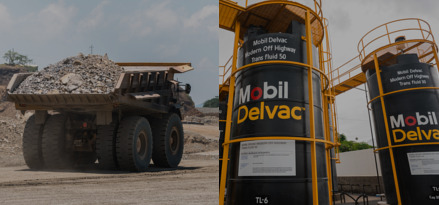 Camión minero con carga en su caja y dos gruas en medio de una mina al aire libre, con una torre de aceite Mobil Delvac.