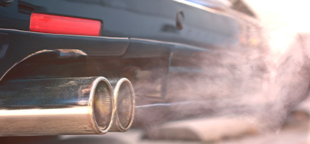 Tubo de escape de un auto sedán expulsando humo blanco.
