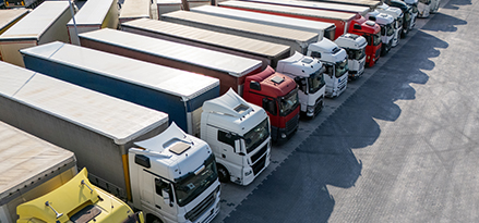 Camiones de carga estacionados uno al lado de otro en un lote de estacionamiento de una nave industrial.