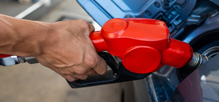 Mano que sostiene una pistola de gasolina en una estacion de servicio para llenar el tanque de su vehiculo.